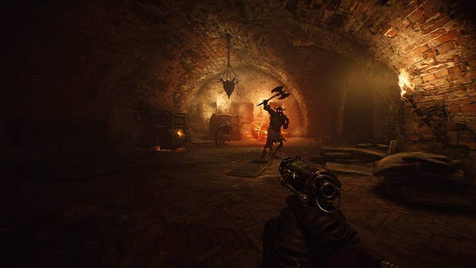 In a moody dungeon, a character wielding a weapon of some kind stands off in the distance, lit from behind with torchlight.