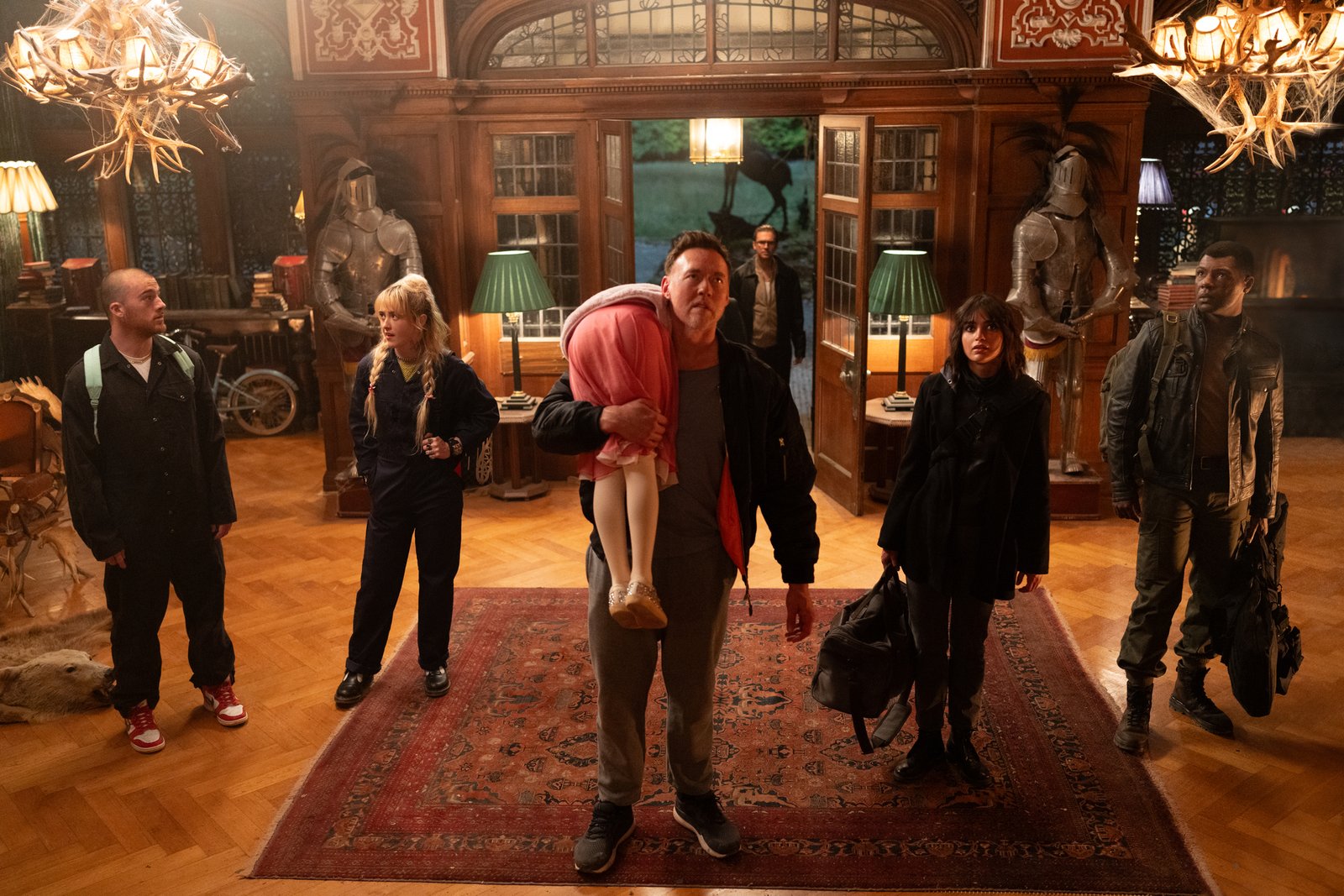 Kevin Durand, Alisha Weir, Kathryn Newton, Dan Stevens, Melissa Barrera, Angus Cloud, and William Catlett stand in the lobby of a fancy mansion in Abigail