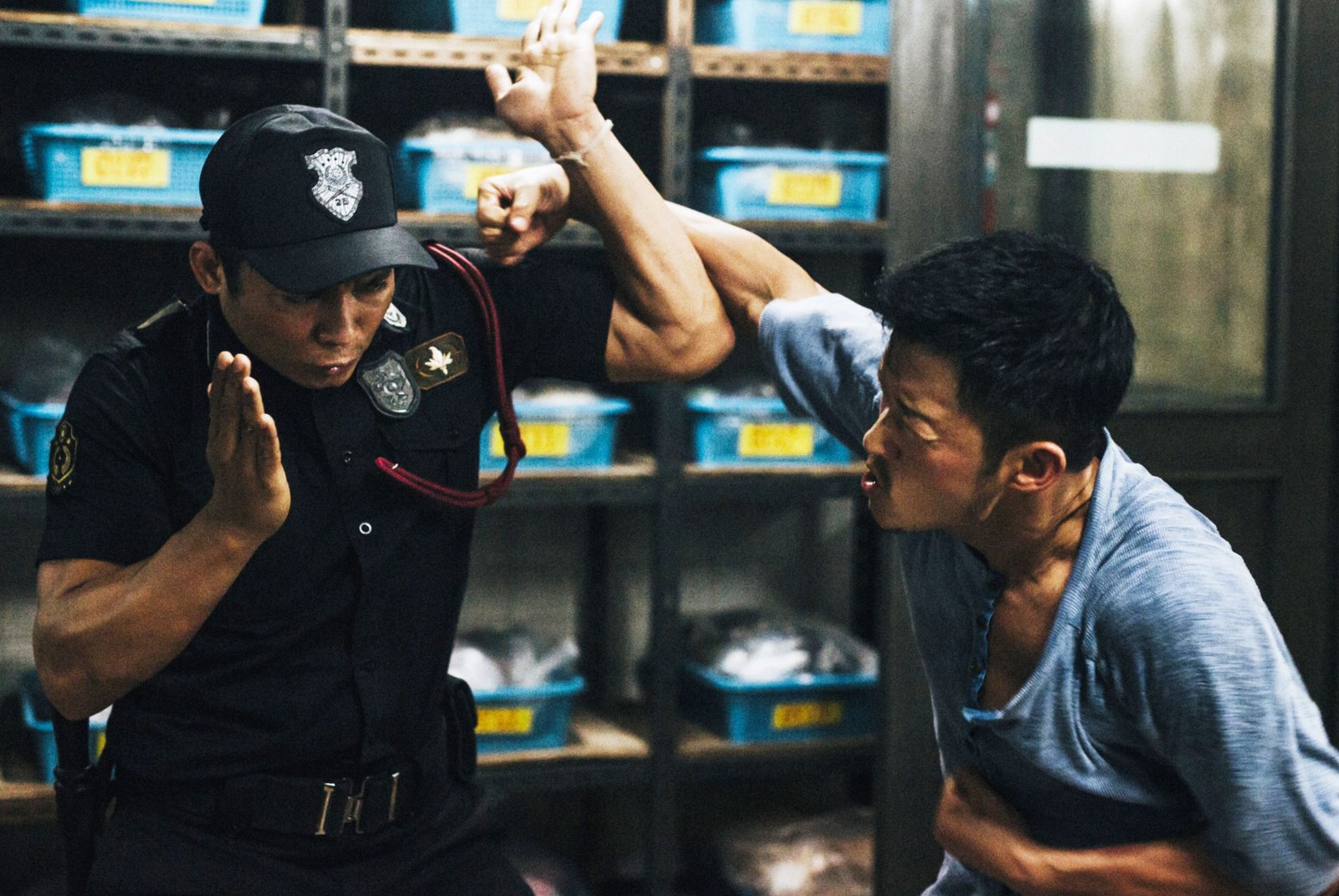 Two men stand in a garage fighting each other. One is wearing a police uniform and blocking a punch from the other who is wearing a blue shirt in SPL 2: A Time for Consequences, aka Kill Zone 2Two men stand in a garage fighting each other. One is wearing a police uniform and blocking a punch from the other who is wearing a blue shirt in SPL 2: A Time for Consequences, aka Kill Zone 2